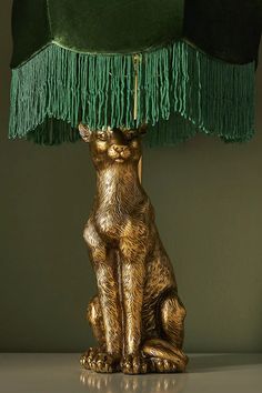 a gold cat sitting under a green lamp on top of a table next to a wall