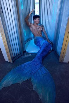 a man sitting on top of a toilet next to a blue mermaid tail