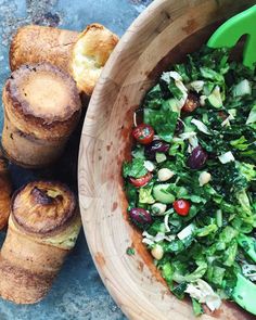 a wooden bowl filled with salad next to rolls