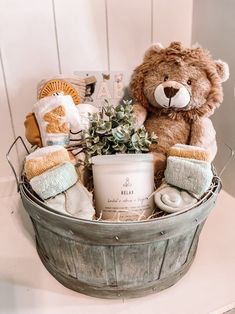 a teddy bear sitting in a bucket filled with blankets and other items next to a baby's name sign