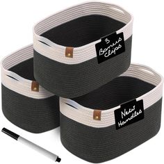 three black and white storage baskets with labels on them, one has a pen in it