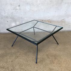 a glass coffee table with metal legs on concrete floor next to white wall and cement surface