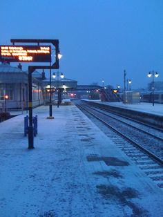 a train station with snow on the ground and tracks in front of it at night