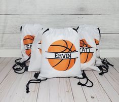 three drawstring bags with basketballs printed on the front and back, sitting on a wooden floor