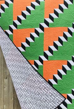 an orange, black and green quilt on a wooden fence next to a piece of fabric