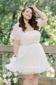 a woman in a white dress posing for a photo on a bridge with her hands behind her head