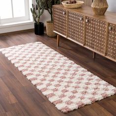 a white and pink rug on the floor in front of a wooden cabinet with potted plants