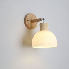 a white wall mounted light with a wooden arm and round shade hanging from it's side