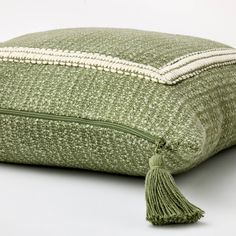 a green and white pillow with tassels on the bottom, sitting on a white surface