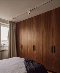 a bedroom with wooden closets and white sheets on the bed in front of a window