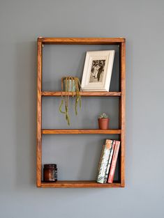 a wooden shelf with books and plants on it against the wall in front of a gray wall