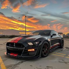 a black sports car parked in a parking lot with the sun going down behind it