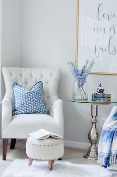 a living room with a white chair, blue and white pillows and a glass table