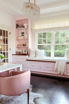 a room with pink furniture and lots of white decor on the windowsill, along with a chandelier hanging from the ceiling