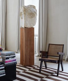 a room with a chair, books and a sculpture in the corner next to a window