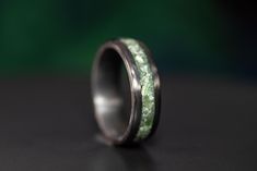 a wedding band with green moss inlays is shown on a black table top