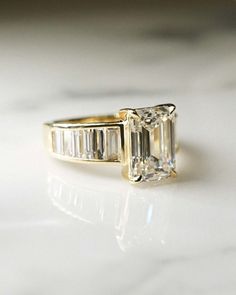 an emerald cut diamond ring with baguettes on the side, sitting on a marble surface