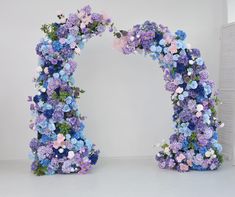 an arch made out of blue and pink flowers is shown in front of a white wall