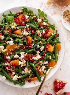 a white plate topped with green beans and pomegranates next to a glass of wine