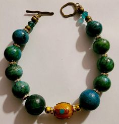 Lovers of Turquoise will recognize the value of these big, bold, chunky and heavy Chrysocolla beads (faux turquoise) which gives you all the dramatic styling without the exorbitant price. This 18" non-adjustable Choker features ten gumball size blue green Chrysocolla beads, each of which is spaced with a brilliant rhinestone rondelle adding light to the piece. A single Tibetan Resin focal bead sits in the front and adds contrast. The back is finished with bronze rounds, faceted crystals and more rhinestone rondelles. Closes with a brass or bronze metal toggle. Makes for a great layering piece with copper, sterling silver, coral or resin. From the Atelier of Kat Kouture. Is dense and adds weight. A reasonable way to treat yourself or gift another. Looks best on a long and thin neck. Please Iris Apfel Style, Necklace Aesthetic, Jewellery Shop Design, Turquoise Western, Turquoise Statement Necklace, Turquoise Bead Necklaces, Beaded Statement Necklace, Western Jewelry, Resin Beads