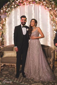 a man and woman standing next to each other in front of a floral arch with lights