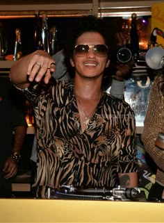 a man wearing sunglasses is sitting at a bar with his hand in the air and another person standing behind him