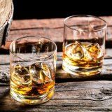 two glasses filled with whiskey sitting on top of a wooden table