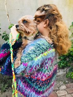 a woman holding a small dog in her arms while wearing a multicolored sweater