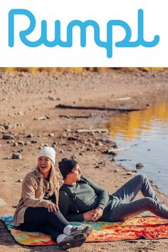 two people are sitting on a blanket by the water with an advertisement for hummus