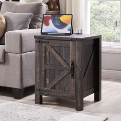 a laptop computer sitting on top of a wooden cabinet in front of a gray couch