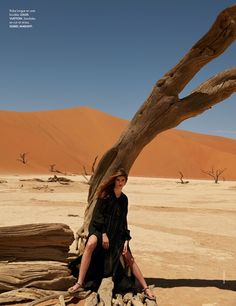 a woman sitting on top of a tree in the middle of an open desert area