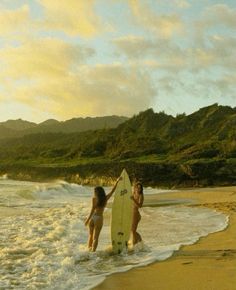 two women walking into the ocean with a surfboard