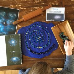 a young boy sitting at a table working on a project with beads and materials around him