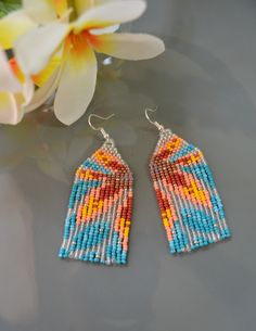 a pair of beaded earrings sitting on top of a table next to a flower