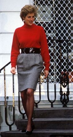 the woman is walking down the steps wearing a red sweater and plaid skirt with black heels