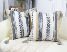 two decorative pillows sitting on top of a white couch next to a potted plant