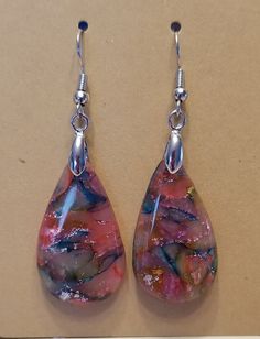 a pair of earrings that have been made with glass and silver wire, hanging from hooks