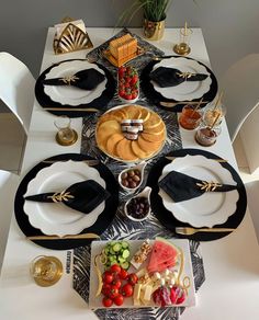 the table is set with black and white plates, gold trimmings, and fruit