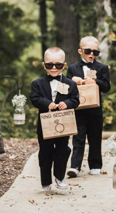 two young boys dressed in black suits and bow ties carrying boxes with ring security written on them