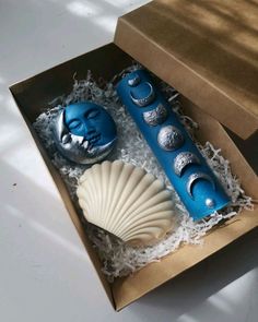 an open box containing two blue candles and a seashell in the middle with white sand underneath