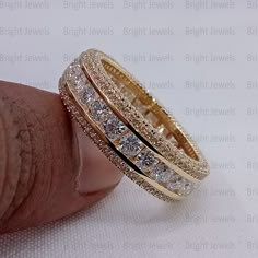 a gold ring with three rows of diamonds on the inside and outside, sitting on top of a finger