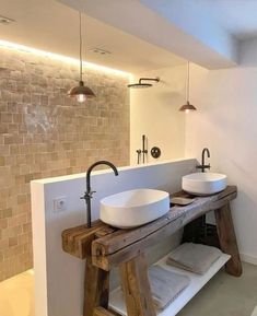 two white sinks sitting on top of a wooden table next to a wall mounted faucet