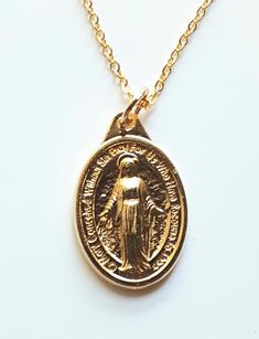 This beautiful gold finished Miraculous Medal is a low cost option for those ladies who prefer to wear gold colored jewelry. The delicate gold finished chain is 18" long, with a lobster jewelry clasp. The medal is approximately one inch tall, which is the standard size for a Miraculous Medal. This pretty piece will keep its bright finish longer if you take it off before showering and freshen it up with jewelry cleaner. The Miraculous Medal was brought to us by Saint Catherine Laboure in 1832, af Gold Plated Jewelry With Miraculous Medal, Gold-plated Jewelry With Miraculous Medal, Gold Locket Necklace With Lobster Clasp As Gift, Gold Miraculous Medal Necklace Gift, Gold Miraculous Medal Pendant Necklace, Gold Pendant Charm Necklace With Miraculous Medal, Gold Oval Pendant Charm Necklace In Brass, Gold Oval Pendant Brass Charm Necklace, Gold Medallion Necklace With Charms As Gift