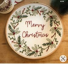 a cross stitch christmas ornament on a wooden table next to a cup and saucer