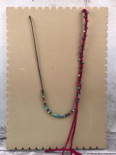 a long beaded necklace with tassels hanging from it's end on a piece of cardboard