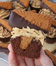 someone holding up a chocolate cupcake with peanut butter frosting