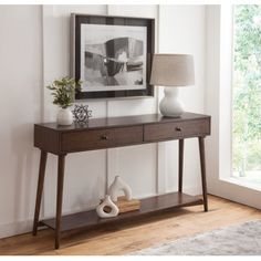 a wooden table with two drawers and a lamp on it in front of a window