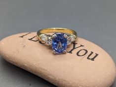 an oval shaped blue sapphire and diamond ring on top of a rock with the words i love you written in cursive writing