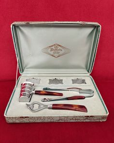 an open box with scissors and other items in it on a red cloth covered surface