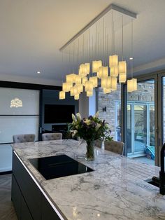 a kitchen island with lights hanging from it's ceiling and flowers in a vase on the counter